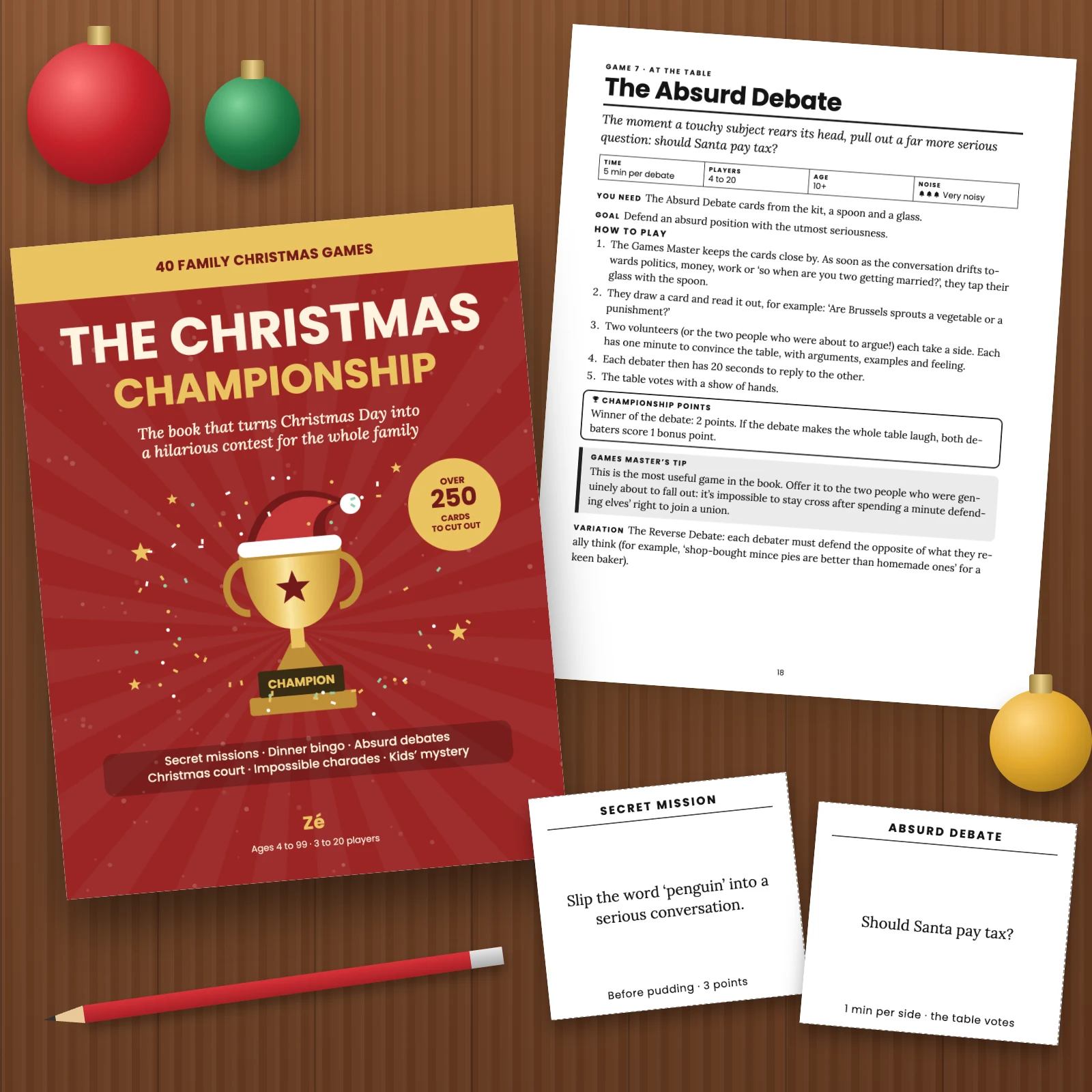 The cover and printed pages of the PDF on a wooden table: the page for game 7 “The Absurd Debate”, a Secret Mission card “Slip the word ‘penguin’ into a serious conversation” and an Absurd Debate card “Should Santa pay tax?”, with Christmas baubles and a pencil