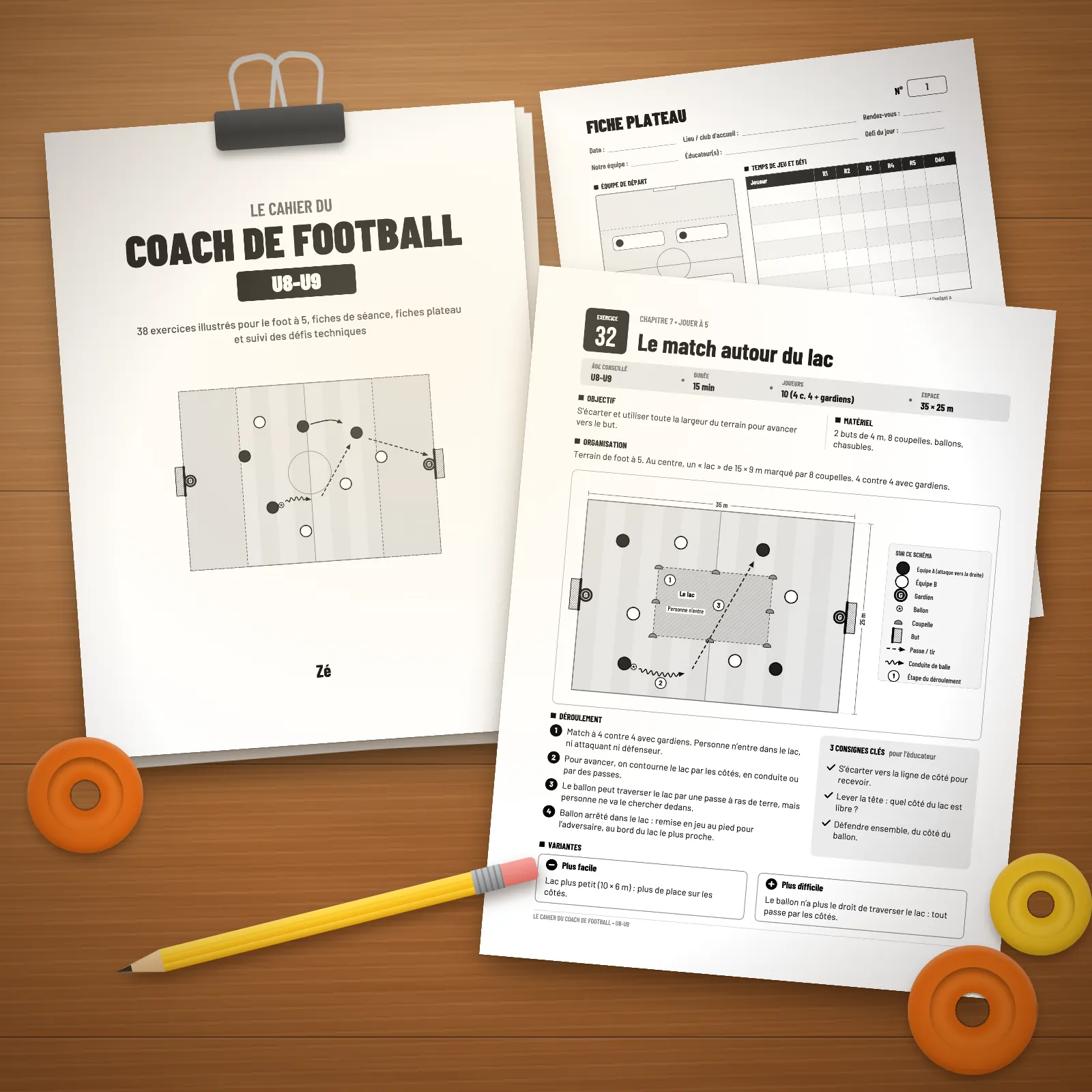 Pages imprimées du cahier U8-U9 sur une table en bois : page de titre tenue par une pince, fiche plateau et exercice n° 32 « Le match autour du lac », avec un crayon et des coupelles