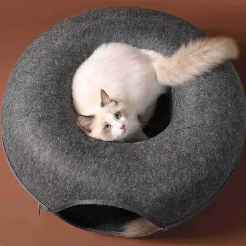 Chat blanc dans un lit en feutre gris foncé en forme de beignet