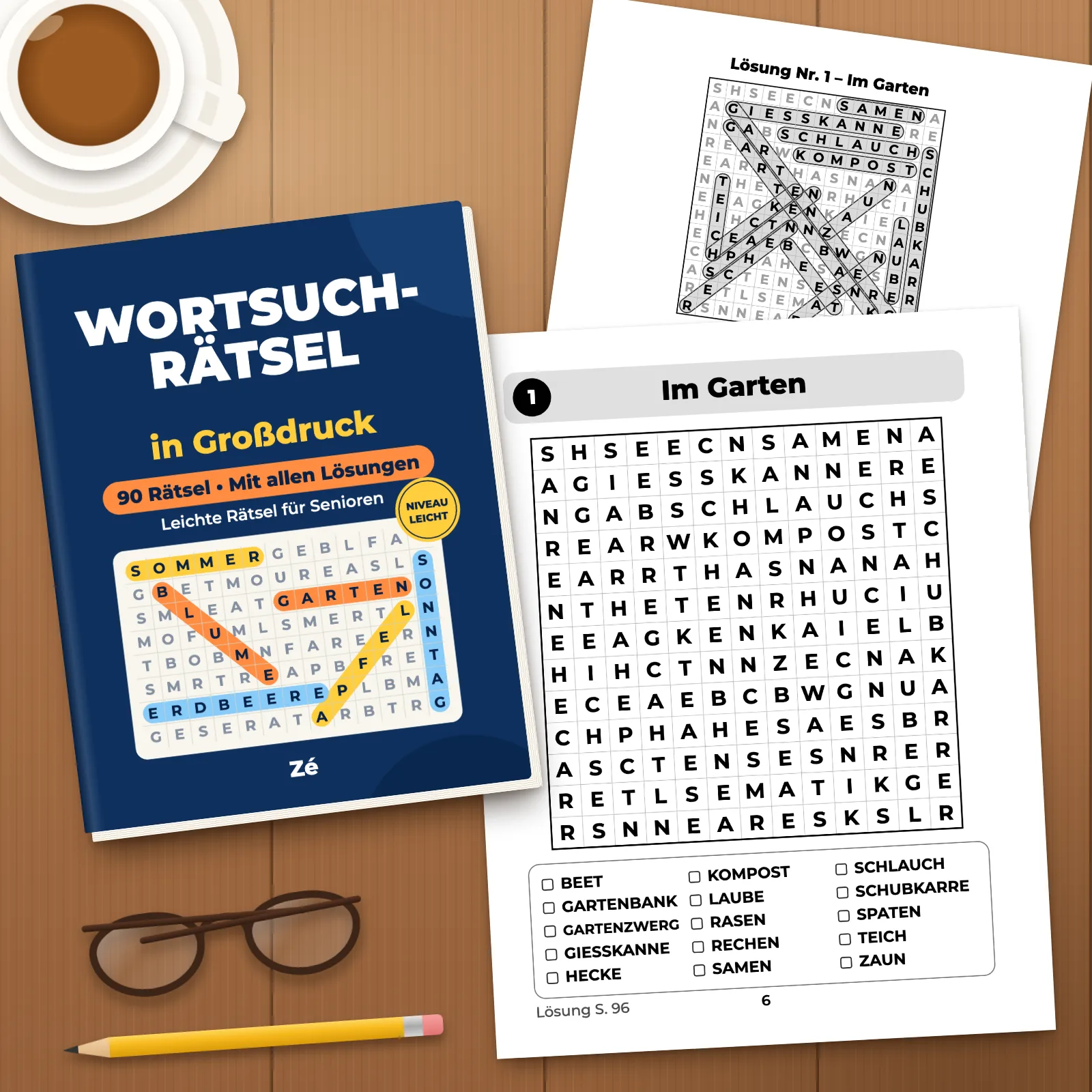 Das Buch auf einem Holztisch mit zwei ausgedruckten Seiten (Rätsel 1 „Im Garten“ und seine Lösung), einer Tasse, einer Brille und einem Bleistift
