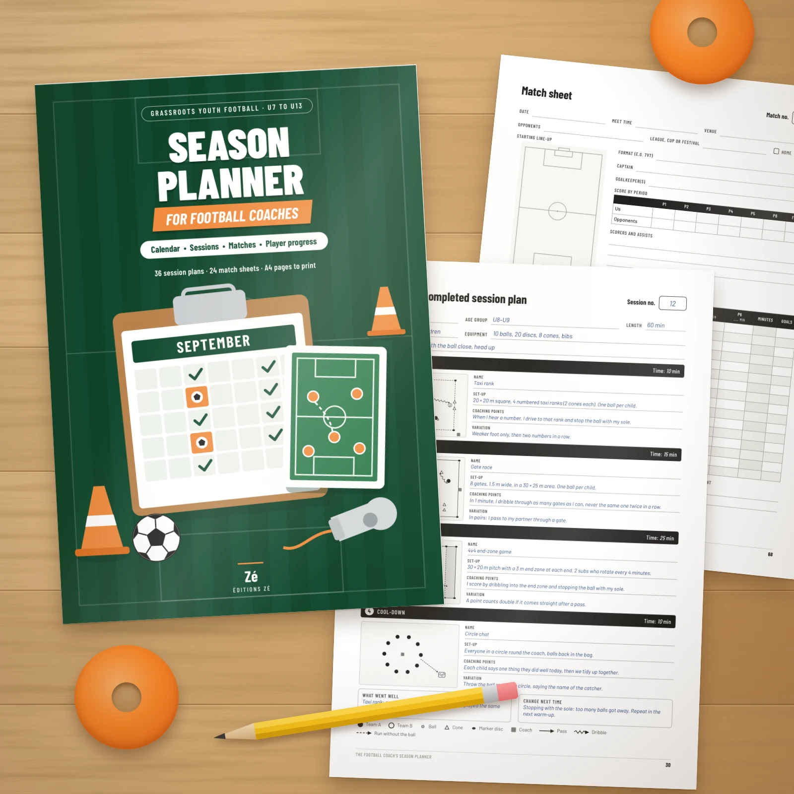 Printed pages of the planner on a wooden table: the cover, a completed session plan and a match sheet, with a pencil and two orange marker discs