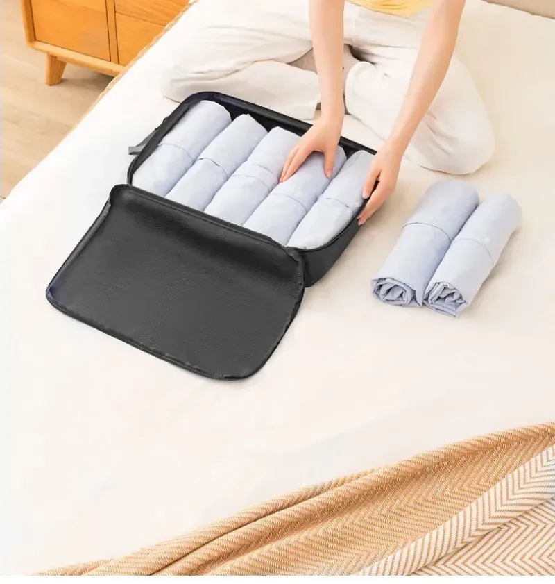 Sac de rangement noir ouvert, rempli de vêtements pliés, posé sur un lit (exemple en noir)